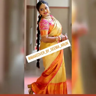 A full-length view of a happy bride ready for her muhurtham. This showcases the complete look, from the expertly draped Kanchipuram silk saree to the traditional long braid hairstyle, ensuring she looks and feels her best.
