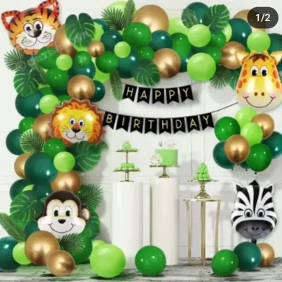 A classic jungle safari themed birthday party. This setup features a green and gold balloon arch, friendly animal face foil balloons including a tiger, lion, and monkey, and pedestals for the cake and treats.