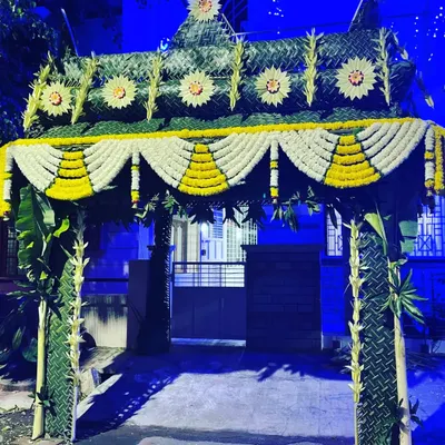 This traditional entrance toran is made from woven coconut leaves and banana stems. The arch is decorated with intricate patterns and garlands of white and yellow flowers, creating a grand welcome for a home ceremony.