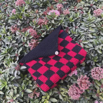 My red and black checkered book sleeve, pictured outside on some bushes. The button flap keeps your book secure inside.