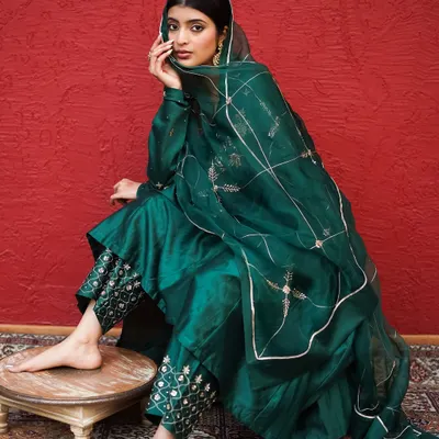 A seated pose that beautifully displays the fall of the emerald green fabric and the detailed embroidery on the pants. The composition draws attention to the craftsmanship of the ethnic attire.