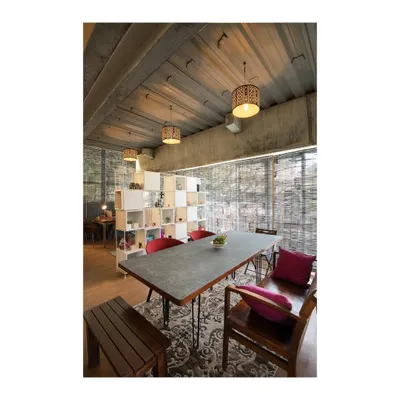 A versatile conference table designed for a gallery and meeting space. The tabletop is made of concrete, providing a durable and textural surface, supported by a simple steel frame. The setup includes a matching wooden bench for flexible seating.