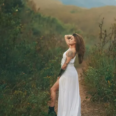 A moment of peace in the wilderness. The model in a flowing white dress against the lush green hills creates a beautiful contrast and a sense of serene escape.