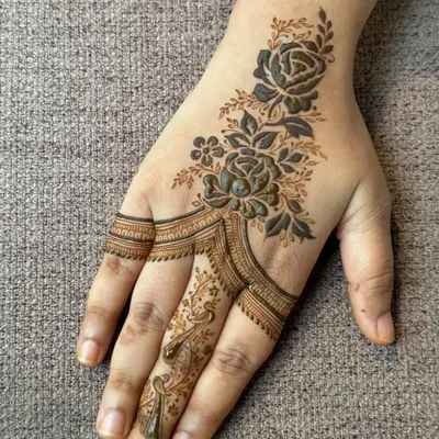 A beautiful and modern rose design. This style, often called a 'haath phool' or hand harness, connects the finger and wrist with a delicate floral trail.