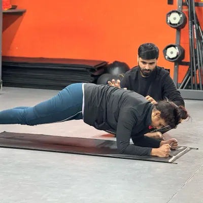 Proper form is crucial for core exercises. Here, a trainer provides tactile cues to help a client maintain a straight back and engage the right muscles during a forearm plank, preventing strain on the lower back.