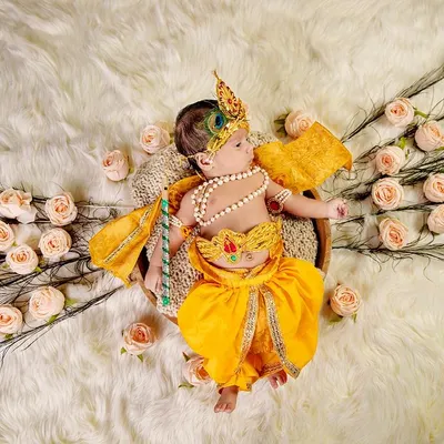 A beautifully styled overhead shot of a newborn dressed as Krishna, surrounded by peacock feathers and roses. Our themed shoots are carefully designed to create stunning, artistic portraits.