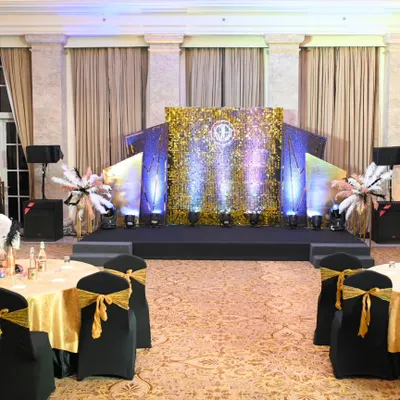 The main ballroom setup for a Great Gatsby themed corporate party. The stage, with its glittering gold backdrop and art deco wings, was the centerpiece, complemented by themed table settings for a cohesive look.