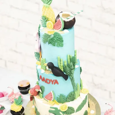 A full view of the three-tiered tropical adventure cake, surrounded by matching flamingo and pineapple cupcakes.