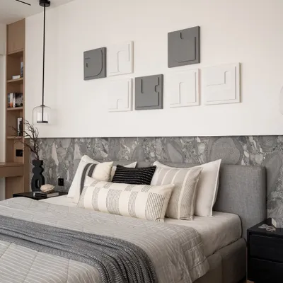 This master bedroom is a serene sanctuary. The bed is framed by an Andromeda leather-finish stone backdrop, complemented by a sleek grey bed and herringbone wood flooring that adds warmth. The textured wallpaper and custom artwork embody quiet luxury in every detail.