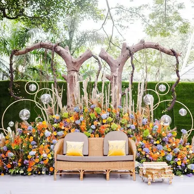 A beautiful and colorful stage for a Mehendi or Haldi ceremony. The design uses a mix of vibrant flowers, pampas grass, and rustic tree branches to create a bohemian and festive look.