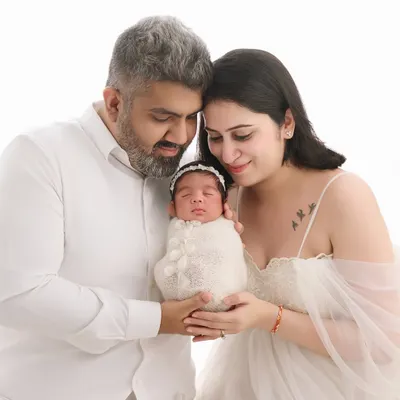 A beautiful family portrait where both parents gaze lovingly at their swaddled newborn, creating a classic and timeless memory in our all-white studio setup.