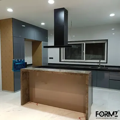 A luxurious open-plan kitchen with a large central island and an integrated chimney. The dark grey back-painted glass cabinets and marble-finish island create a dramatic and sophisticated focal point in the home.