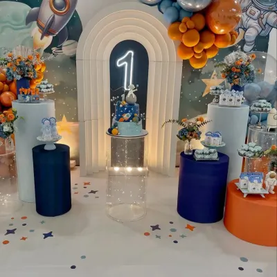 Our space-themed parties are an adventure for the imagination. This setup for a first birthday includes a galaxy backdrop, a rocket ship, planet-themed desserts, and a glowing number '1'.
