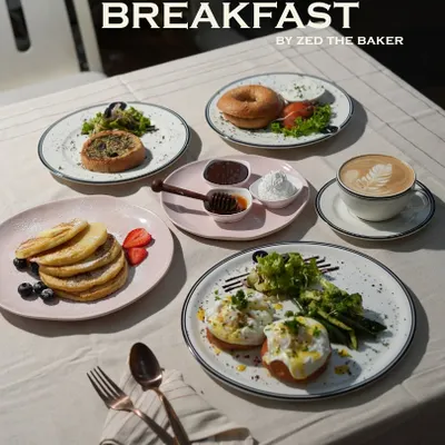 A glimpse of the perfect breakfast spread. It features fluffy pancakes with fresh berries, classic eggs benedict, a savory bagel, and a freshly brewed cappuccino to start your day right.
