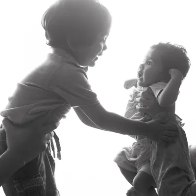 A black and white version of this sweet sibling interaction. The monochrome edit adds a timeless, classic feel to the moment, focusing on the expressions and the connection between them.