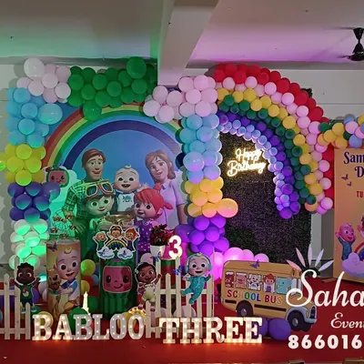 A full-scale Cocomelon themed birthday party. This vibrant setup includes a rainbow balloon arch, character cutouts, a themed backdrop, and even a yellow school bus prop for a completely immersive experience.