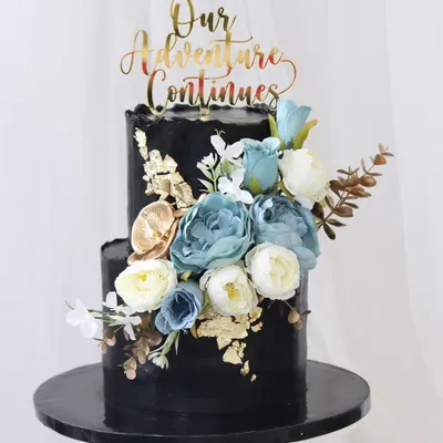 A breathtaking black two-tiered wedding cake that exudes modern elegance. The deep black fondant provides a dramatic backdrop for the cascade of blue and white sugar flowers, accented with gold leaf for a touch of luxury.
