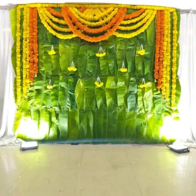 A classic Haldi setup with a backdrop made entirely of fresh banana leaves. The top is decorated with bright yellow and orange marigold garlands, creating a traditional and auspicious look.