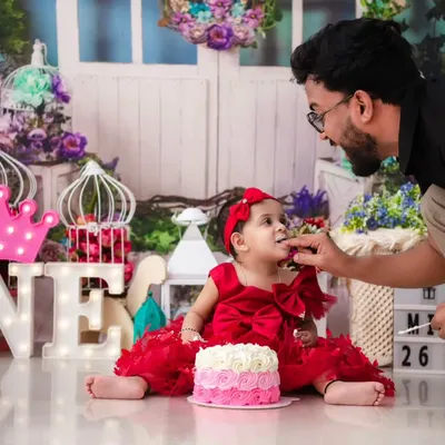 The first taste of birthday cake. This wide shot captures the full first birthday setup, with "ONE" marquee lights and a proud father sharing a sweet moment with his daughter.