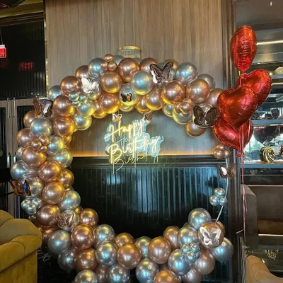 This elegant ring backdrop is made with metallic chrome balloons in silver and rose gold, accented with butterfly details. The neon "Happy Birthday" sign adds a modern touch.