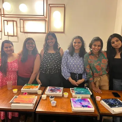 A group of friends proudly displaying their colorful fluid art canvases. Our paint and sip events are a great way to catch up while creating something beautiful and abstract.