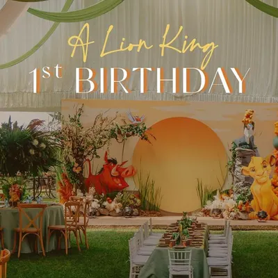 A wide shot of a Lion King first birthday celebration set up in a large outdoor tent. The design features a fully realized Pride Rock backdrop, themed table settings on the lawn, and dramatic fabric draping on the ceiling to mimic the sky.
