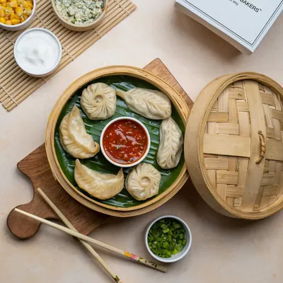 An assortment of our handcrafted momos, featuring both classic pleated and round shapes, served in a traditional bamboo steamer. This platter shows the variety of fillings and styles we offer.