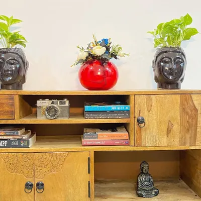 The apartment is filled with unique decor pieces, like this wooden cabinet with books, plants, and Buddha statues to create a calm and welcoming vibe.