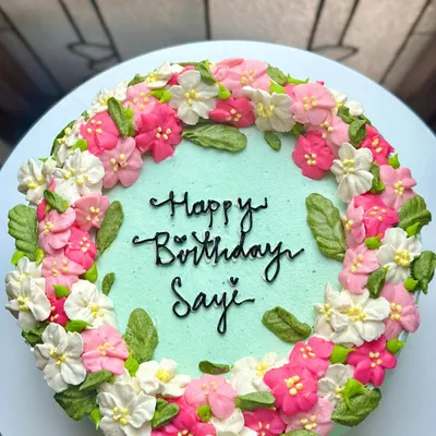 This shows the incredible detail we can achieve with buttercream flowers on a larger cake. This birthday cake for Sayi features a wreath of hand-piped pink and white blossoms on a mint-green base.