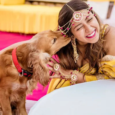 A bride shares a laugh as her cocker spaniel gives her an affectionate lick during the Haldi ceremony. This is a perfect, candid moment of love between a girl and her dog.
