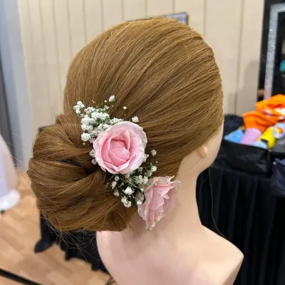 A classic and romantic bridal updo. This beautifully structured bun is adorned with delicate pink roses and baby's breath, perfect for a wedding or reception.