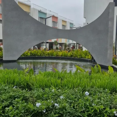The water and concrete sculpture seen during the day. The strong, curved forms of the concrete contrast with the soft texture of the surrounding aquatic plants, creating a balanced and visually engaging composition.