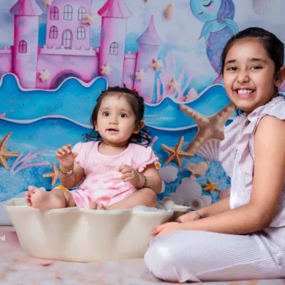 An enchanting "Under the Sea" photoshoot with two sisters. The little one sits in a clamshell while her older sister smiles beside her, creating a magical mermaid memory.