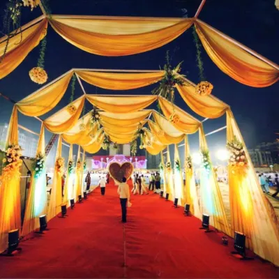 A spectacular wedding entrance walkway with a red carpet, covered by a canopy of golden drapes and lit by spotlights, creating a glamorous path for guests.