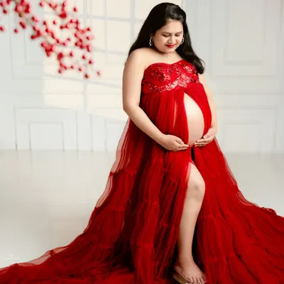 A bold and beautiful portrait in a stunning red tulle gown. The open-front design tastefully showcases the baby bump, celebrating the beauty of the pregnant form.