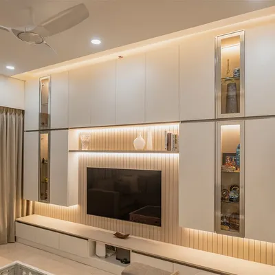 This full-wall entertainment unit is a masterpiece of functional design. It features a mix of closed cabinets, open shelves, and glass display sections, all beautifully illuminated with integrated LED lighting.