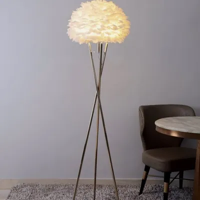 This modern Nordic standing lamp features a lush white feather shade on a sleek tripod base. It is designed to be a source of soft, diffused light, perfect for creating a cozy and serene atmosphere in a living room or bedroom.