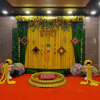 A beautiful Haldi setup with a yellow and green theme, featuring a large lotus-shaped bowl for the ceremony, marigold garlands, and traditional Rajasthani umbrellas.