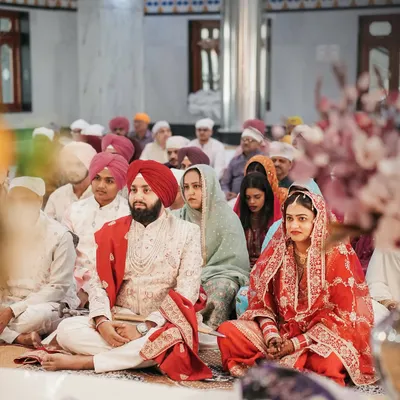 A wide shot of the couple during the Anand Karaj ceremony, surrounded by their family and friends in the Gurudwara. We capture the community and spiritual atmosphere of a Sikh wedding.