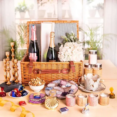 This is the ultimate luxury wedding hamper, overflowing with treats for the new couple. It includes two bottles of champagne, agate coasters, candles, gourmet snacks, and decorative items, all packed in a classic wicker basket.