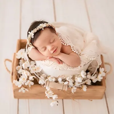 A perfect example of a classic newborn portrait. The baby is posed safely in a white bucket, surrounded by delicate flowers, with a gentle smile that melts your heart. This style is truly timeless.