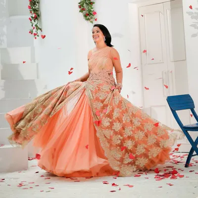 A client having fun in a stunning peach Shantanu & Nikhil rental gown. The attached, heavily embroidered drape adds drama and elegance, making it a showstopper for any evening event.