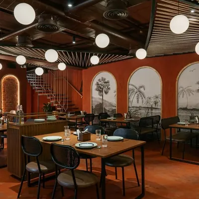 The 'Chambal' restro-bar features an open-plan dining area with a monochromatic red color scheme and rustic brick walls. The design creates a warm, energetic atmosphere perfect for a modern Indian restaurant.