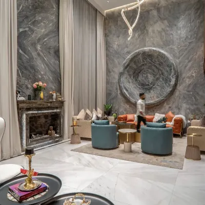 A view of the double-height living room, showcasing the grand scale and material richness. The design features a marble-clad fireplace, elegant drapery, and a curated selection of furniture that balances comfort with sophisticated style.