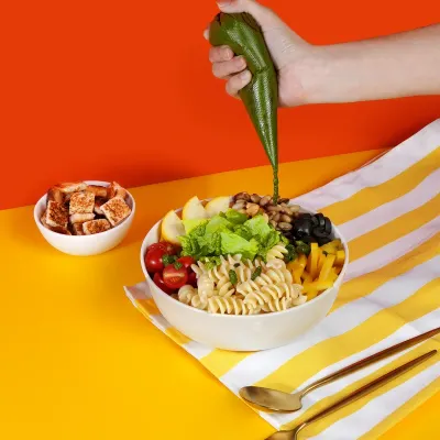 Our Pesto Piccolo bowl getting its final touch. The vibrant pesto dressing brings together pasta, fresh greens, and crunchy toppings for a meal that's bursting with energy.