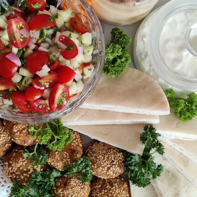 A close-up of the fresh components of our Mezze Platter. You can see our sesame-coated falafel, fresh Israeli salad, soft pita bread, and creamy dips, all ready to be assembled and enjoyed.