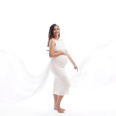 Capturing the pure joy and anticipation of motherhood with a classic, bright white studio setup. The flowing fabric adds a touch of angelic grace to this beautiful maternity portrait.
