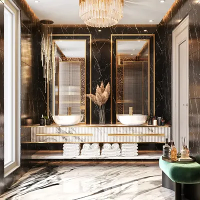 A luxurious bathroom featuring a floating dual-sink vanity set against a black marble wall with gold-framed mirrors. A cascading chandelier and green velvet stool add touches of opulence.