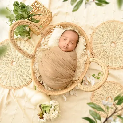 An overhead shot of a newborn in a wicker basket, surrounded by natural textures and greenery. This boho-inspired flat-lay is artistic and beautifully composed.