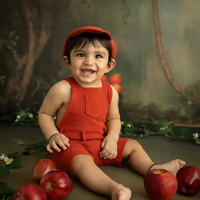 An adorable 8-month milestone session with an apple orchard theme. This little one's happy grin and bright red outfit make for a joyful and vibrant portrait.
